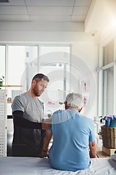 Assessing the situation. a young male physiotherapist assisting a senior patient in recovery.