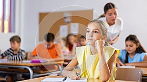 Assiduous focused tween girl sitting with pen and notebook at lesson