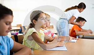 Assiduous focused tween girl sitting with pen and notebook at lesson