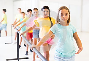 Assiduous preteen girl working near ballet barre during group choreography class