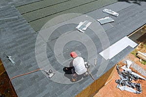 With assistance an air nail gun, professional roofing contractor installed new asphalt bitumen shingles on roof of a