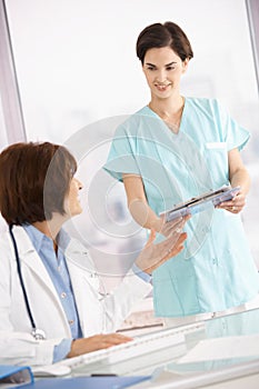 Assistant handing over clipboard to doctor