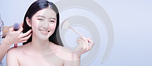 Assistant hands help to make hair salon for young asian woman with half naked applying cosmetic powder brush on smooth face,