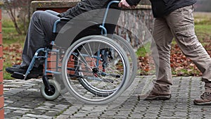 Assistant pushing the wheelchair with disabled man on the sidewalk