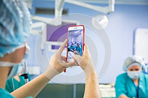 Assistant shooting on the smartphone from the operating room. Medical Team Performing Surgical Operation in Modern