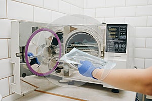 Assistant with sterile dentist tools. Sterilizing medical instruments in autoclave. Dental office