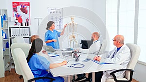 Assistent pointing on skeleton in front of medical stuff