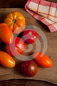 Assort of different shape and color tomatoes on wooden background with red kitchen towel