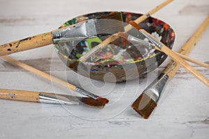 Assorted art paintbrushes randomly placed wooden paint mixing bowl creative background