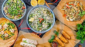 Pho ga, pho bo, noodles, spring rolls, salad with shrimps and mango on black stone table top view