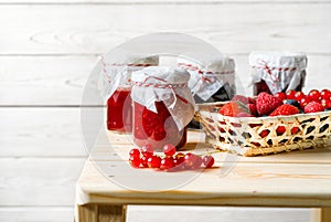 Assorted berries in a basket, glass jars with jams from different berries