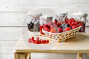 Assorted berries in a basket, glass jars with jams from different berries