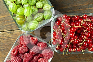 Assorted berries of raspberries, gooseberries and red currants in glass bowls on a wooden table.