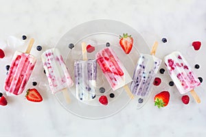 Assorted berry fruit yogurt popsicles, top view in a row over marble