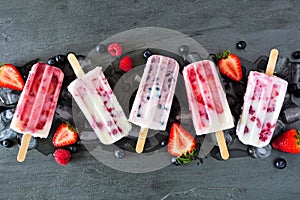 Assorted berry fruit yogurt popsicles, top view in a row over slate