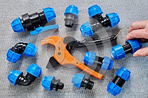 Assorted Blue Polyethylene Pipe Fittings and an Orange PVC Pipe Cutter on a Grey Background