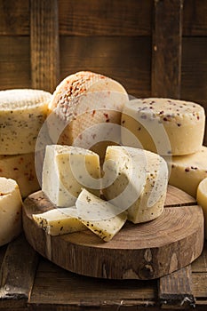 Assorted caciotta cheese on wooden board on dark background