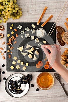 Assorted with cheese , fruits and nuts on the black stone with woman hand