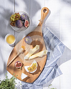 Assorted cheeses with figs, grapes and honey on a wooden board on white background with fresh herb. Healthy and delicious snacks