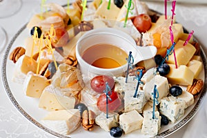 Assorted cheeses, grapes and nuts on a plate with honey. appetizers