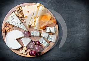 Assorted cheeses, nuts and grapes on a black background