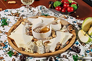 Assorted cheeses on round wooden board plate served with white wine Guda cheese, cheese grated bark of oak, hard cheese slices,