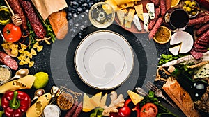 Assorted cheeses, sausages, wines, traditional spices and fresh vegetables on a wooden background.