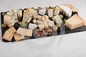 Assorted cheeses with white grapes, walnuts, crackers and on a stone Board. Food for a romantic date on a light background