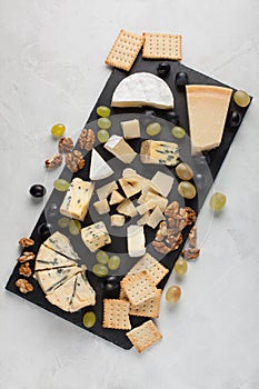 Assorted cheeses with white grapes, walnuts, crackers and on a stone Board. Food for a romantic date on a light background. Top vi