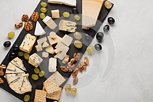 Assorted cheeses with white grapes, walnuts, crackers and white wine on a stone Board. Food for a romantic date on a light backgro