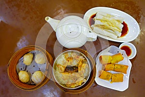 Assorted Chinese food set, dumplings, and rice noodle rolls, famous Chinese cuisine dishes on a wooden table, top view. Chinese re