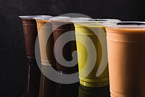 Assorted colorful iced cafe drinks in plastic cups lined up against a textured dark black background