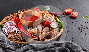 Assorted delicious grilled meat and sausages with tomatoes and bbq sauce on cutting board over black stone background