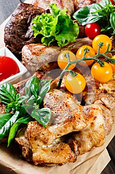 Assorted delicious grilled meat and vegetables with fresh salad and bbq sauce on cutting board on wooden background