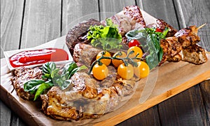 Assorted delicious grilled meat and vegetables with fresh salad and bbq sauce on cutting board on wooden background close up