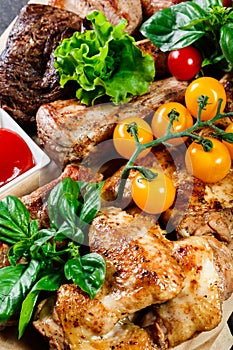 Assorted delicious grilled meat and vegetables with fresh salad and bbq sauce on cutting board on wooden background close up. Big