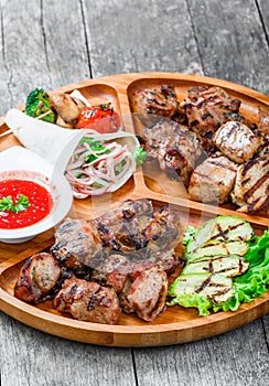 Assorted delicious grilled meat and vegetables with fresh salad and bbq sauce on cutting board on wooden background close up