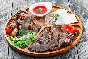 Assorted delicious grilled meat and vegetables with fresh salad and bbq sauce on cutting board on wooden background