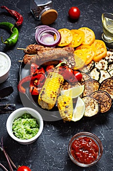 Assorted delicious grilled vegetables and meat on a dark stone background. Summer food