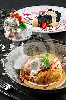 Assorted desserts with tasty apple strudel with ice cream, black cheesecake and jar of ice cream with fruits on dark wooden