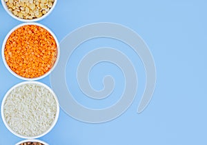 Assorted different cereals on a blue background. Buckwheat, lentils, rice, peas in plates top view