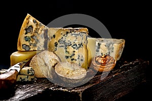 Assorted different luxury gourmet cheeses on a wooden board on a dark background. Various types of cheese: hard and soft with mold