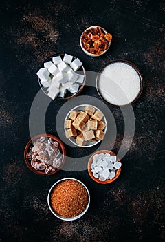 Assorted different types of sugar in bowls on a table on a dark background, vertical image