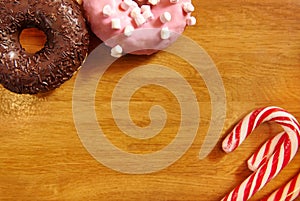 Assorted doughnuts with sprinkles and Christmas candy cane on a wooden surface. Background with copy space