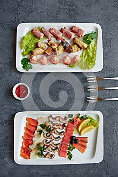 Assorted fish, red fish canapes, eggplant and ham rolls stuffed with cheese and herbs on a white plate on a gray background