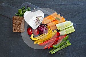 Assorted fresh chopped vegetables with dip on dark background, tasty and healthy snack