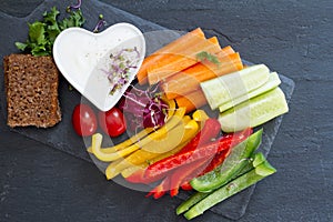 Assorted fresh chopped vegetables with dip on dark background, tasty and healthy snack