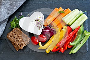 Assorted fresh chopped vegetables with dip on dark background, tasty and healthy snack