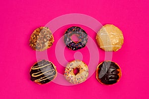 Assorted fresh donuts on a pink background