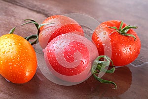 Assorted fresh tomatoes with green leaves on wooden background